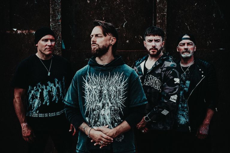 Heavy metal band Bullet For My Valentine members pose together in dark streetwear, with frontman Matt Tuck in the center.